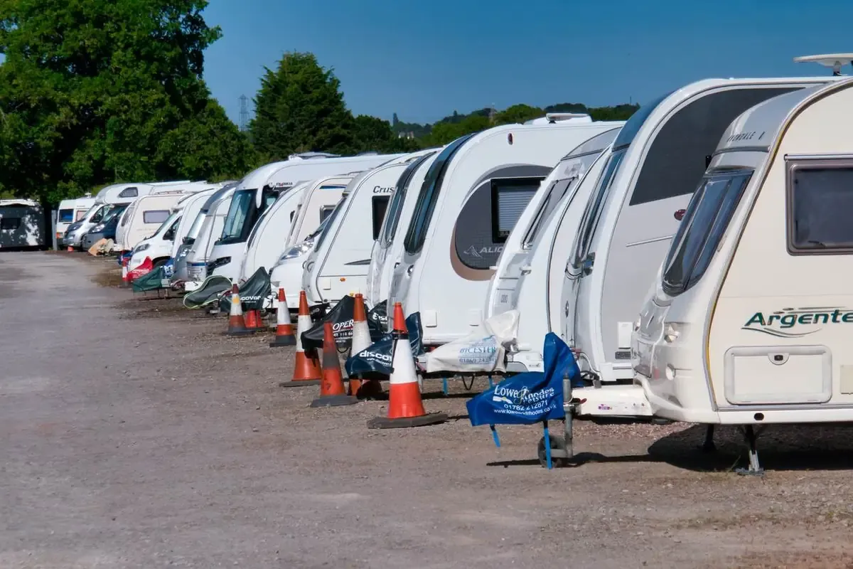 White trailers and RVs are parked in a line in a parking lot on a sunny day.
